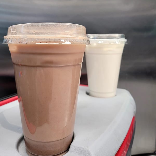 Two plastic cups of Taquiza Street horchata, one chocolate and one classic, on a gray surface.