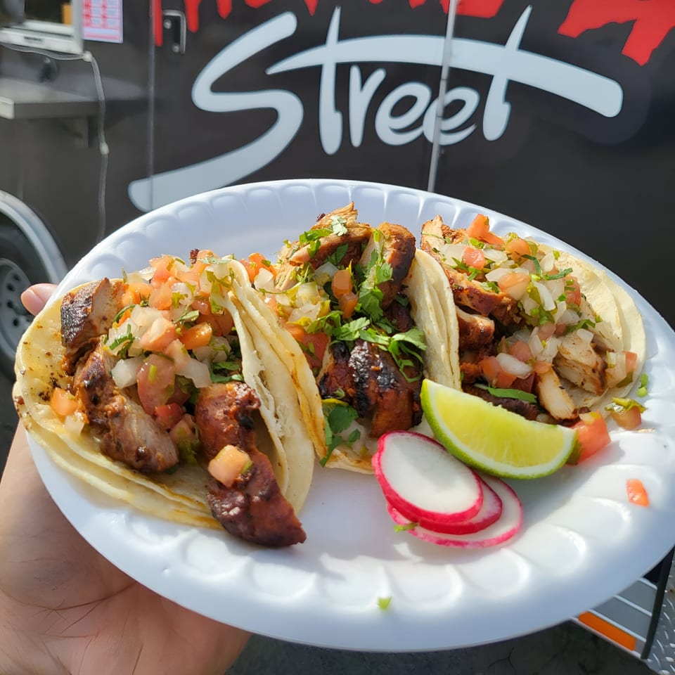 Three chicken tacos with pico de gallo, cilantro, lime, and radishes on a white plate.