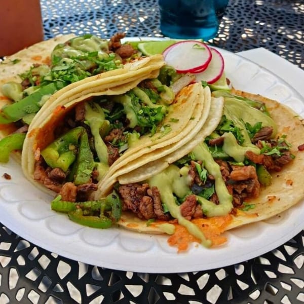 Three Taquiza Street tacos with meat, green peppers, cilantro, and sauces on a white plate.