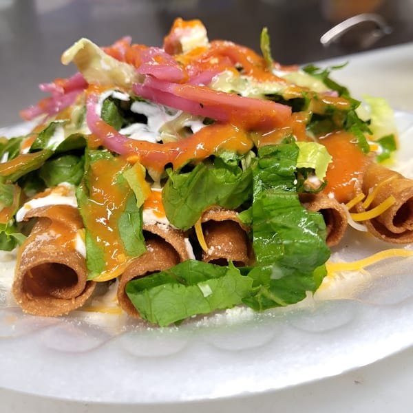 Taquiza Street's taquitos topped with fresh lettuce, pickled onions, sour cream, and orange sauce.