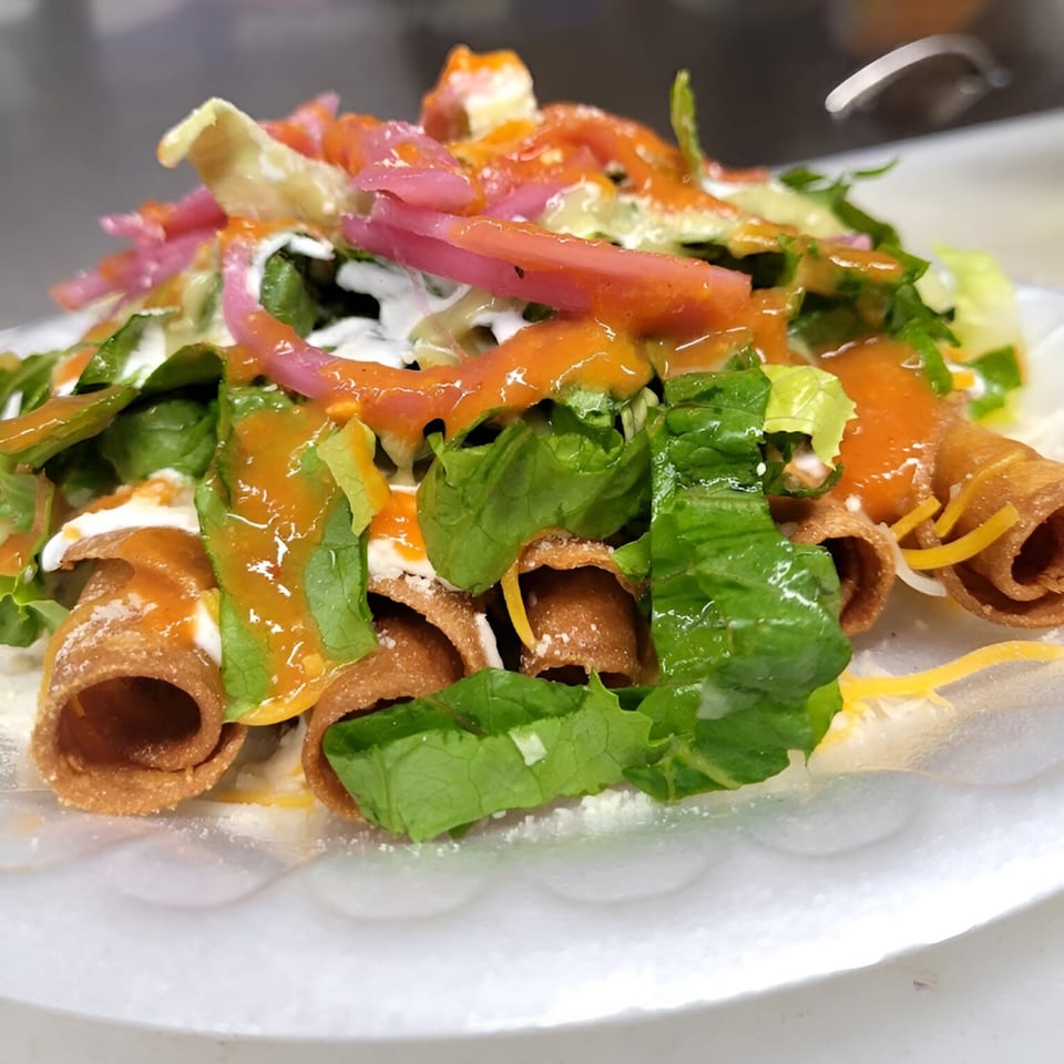 Taquiza Street's taquitos topped with fresh lettuce, pickled onions, sour cream, and orange sauce.