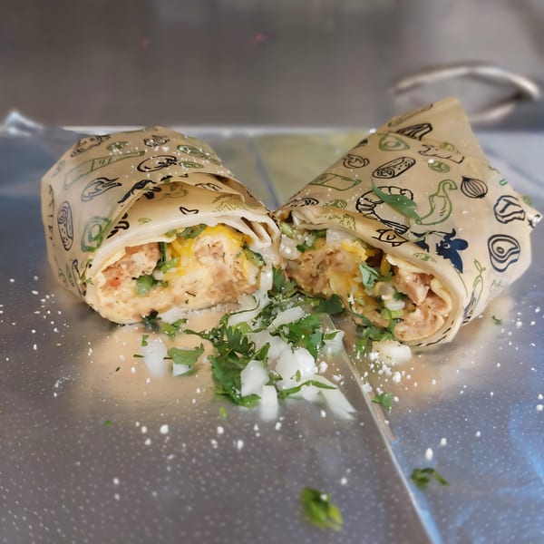 A Taquiza Street burrito, cut in half, revealing chicken, cheese, cilantro, and onions.