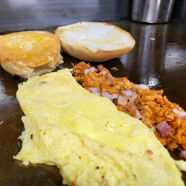 Mexican street food cooking on a griddle, with buns, scrambled eggs, and diced meat.