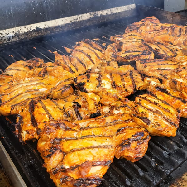 Marinated chicken pieces with grill marks cooking on a smoky, hot grill at Taquiza Street.