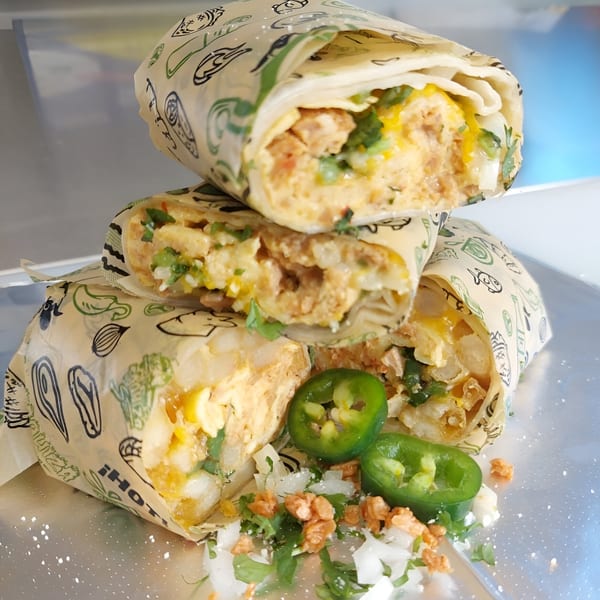 Three Taquiza Street burritos, filled with meat and cheese, garnished with jalapeños, onions, and cilantro.