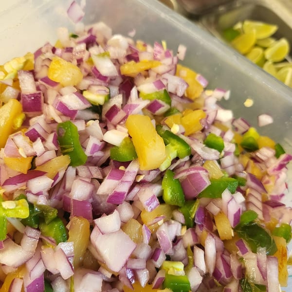 Close-up of diced red onions, green peppers, and yellow pineapple in a clear container.