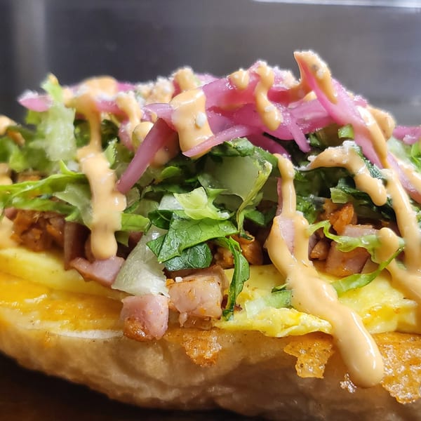 Close-up of a Mexican torta with scrambled eggs, meat, lettuce, pickled onions, and sauce.