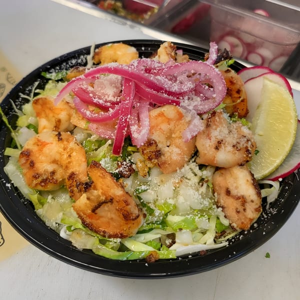 Taquiza Street's shrimp salad with pickled red onions, cheese, lime, and radishes in a black bowl.