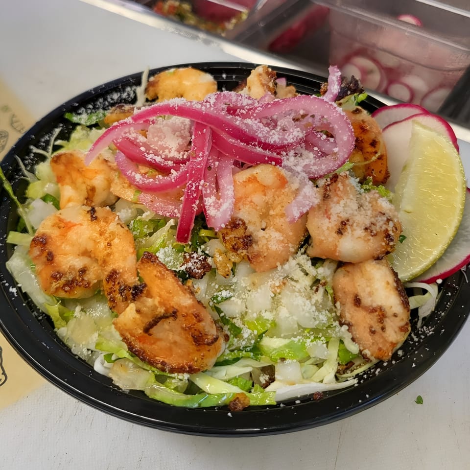 Taquiza Street's shrimp salad with pickled red onions, cheese, lime, and radishes in a black bowl.